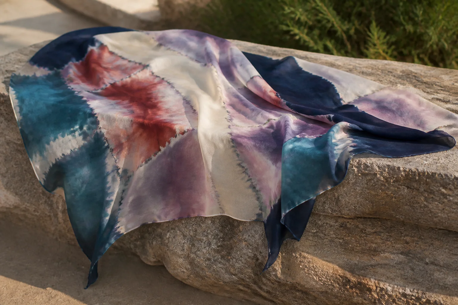 Abstract resist-dyed silk scarf draped over a stone bench
